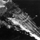 A photograph taken by the crew of a US Navy Grumman TBM Avenger dive bomber shows the Japanese carrier Zuiho on fire during the Battle of Cape Engano. Note the buckled flight deck from fires belowdecks, and the false guns and bow painted on the deck to disguise the carrier. Zuiho later sank during the battle. (US Navy)